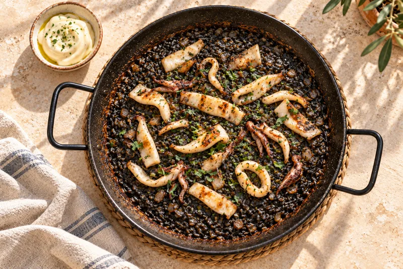 Arroz negro con calamar a la plancha en paella de hierro y un cuenco de alioli