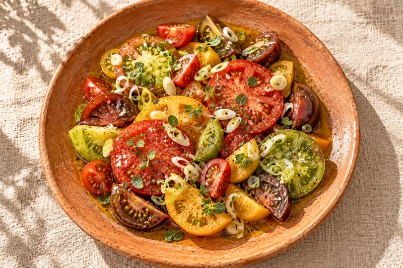 Ensalada de tomates de colores con cebolleta, aceite de oliva y orégano en un plato de barro